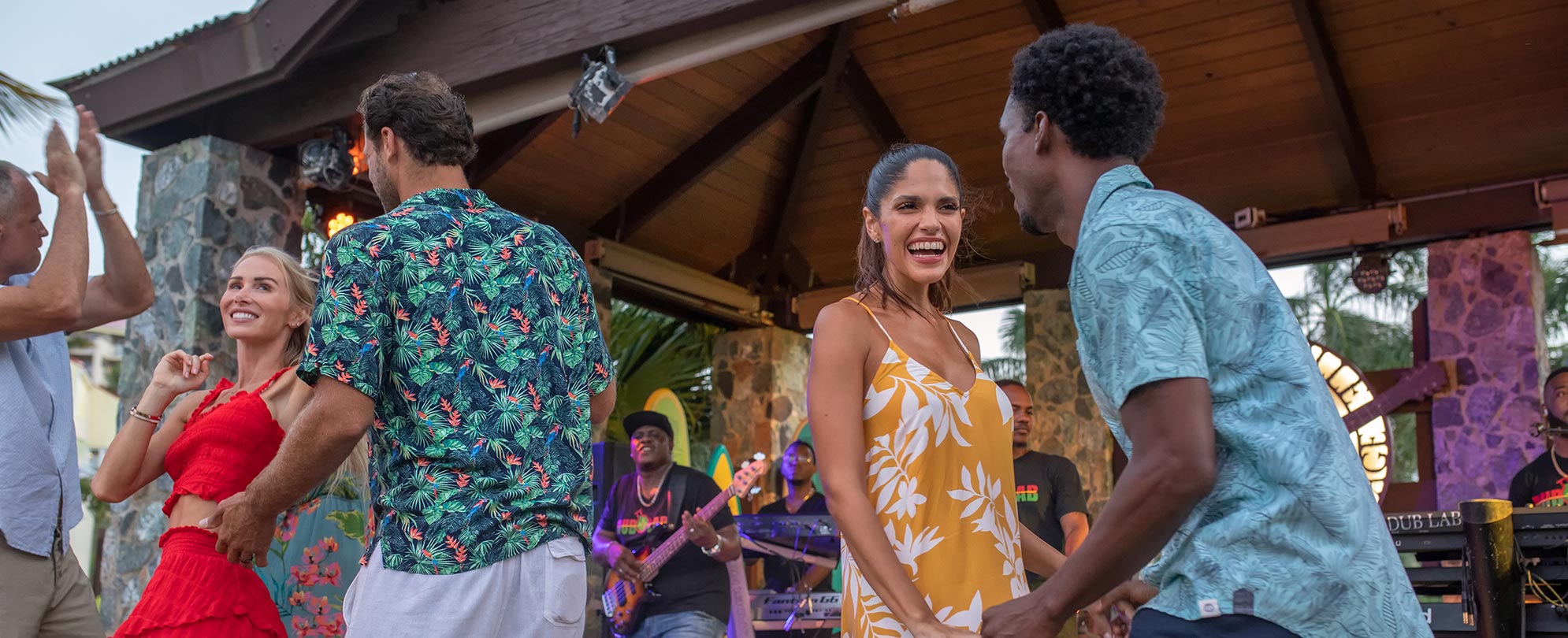 Men and women enjoy a warm winter vacation, dancing in front of a live band at a Margaritaville Vacation Club resort.